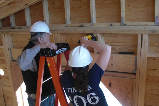 Photo of mentor Charlie Berliner helping team leader Leah Davies use a saw
